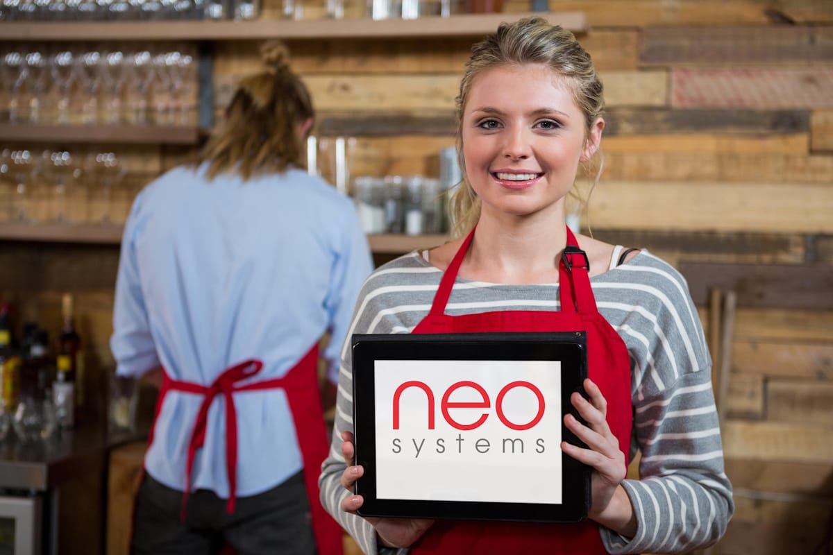 Commerçante souriante tenant une tablette avec le logo Neo Systems, illustrant un logiciel de caisse certifié NF 525