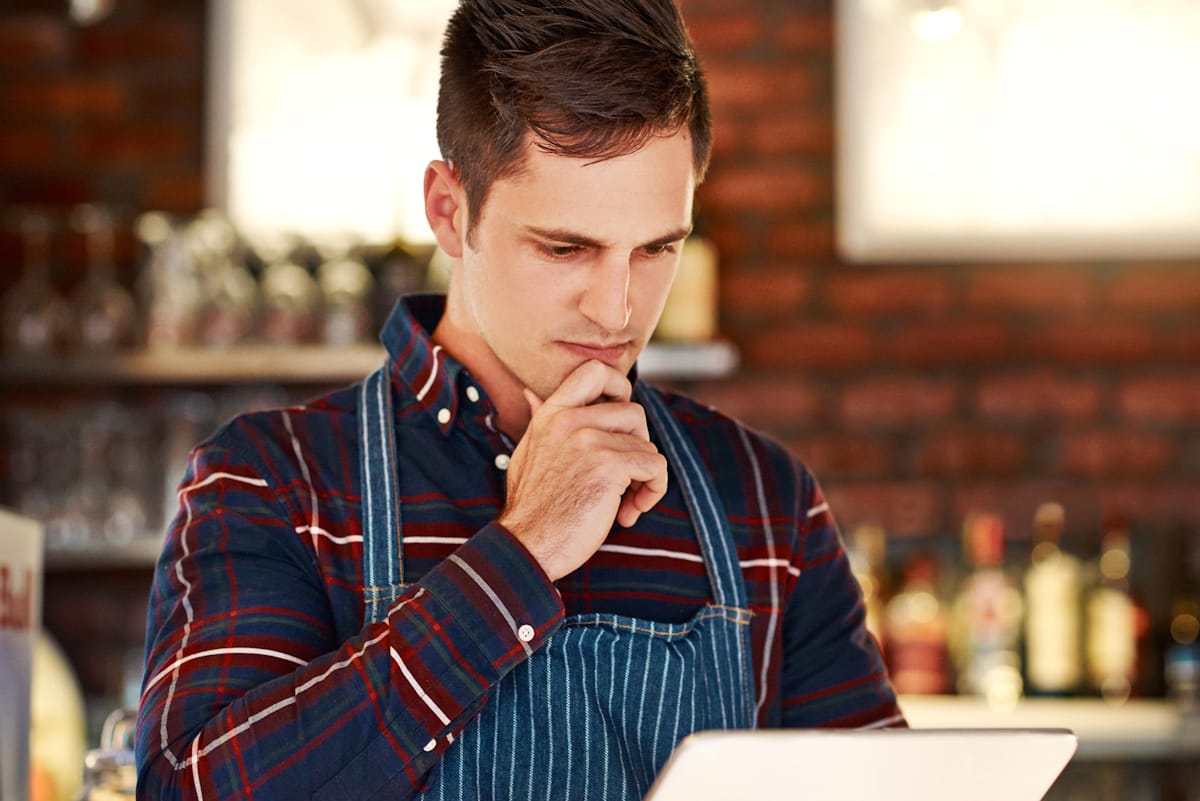 Jeune homme en réflexion devant une tablette, symbolisant le choix d'un logiciel de caisse certifié et adapté