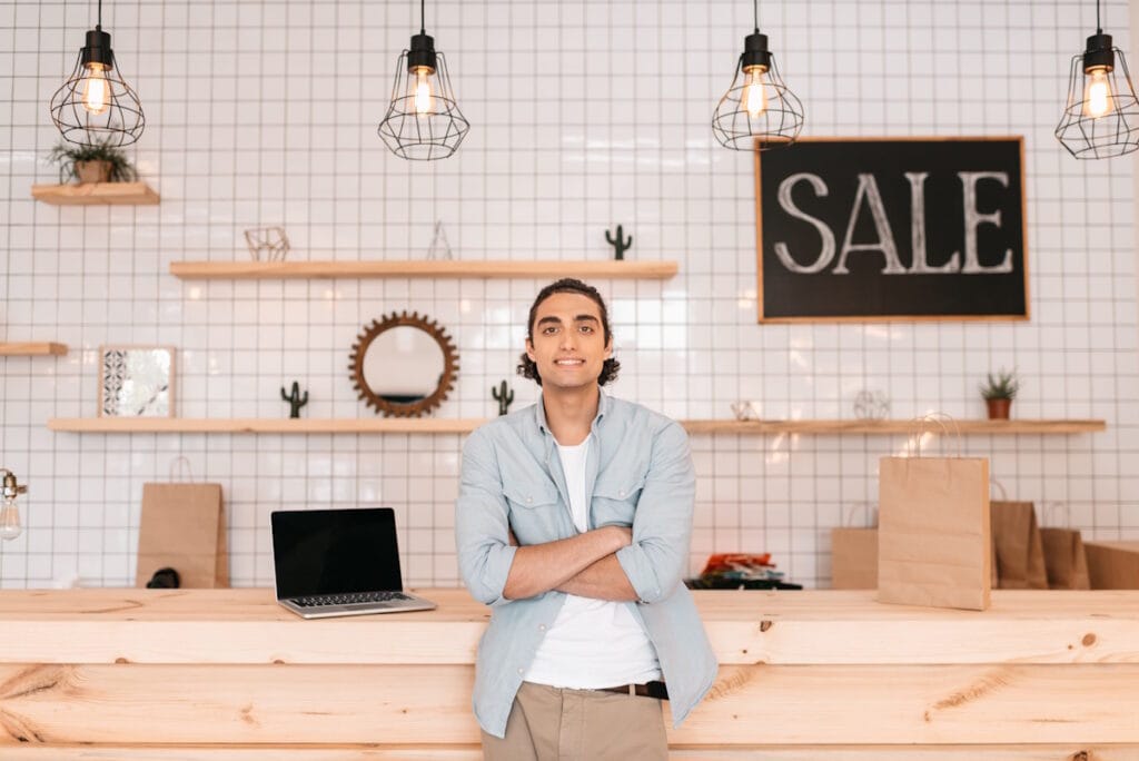 Jeune homme confiant et souriant devant le comptoir de son commerce