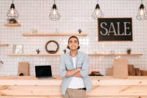 Jeune homme confiant et souriant devant le comptoir de son commerce
