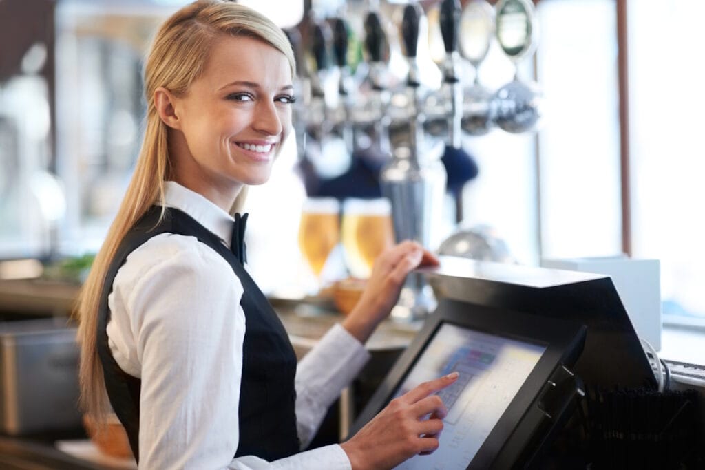 Jeune serveuse souriante derrière une caisse tactile