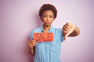 Jeune femme dépitée, le pouce tendu vers le bas tenant un écriteau marqué "Sale"
