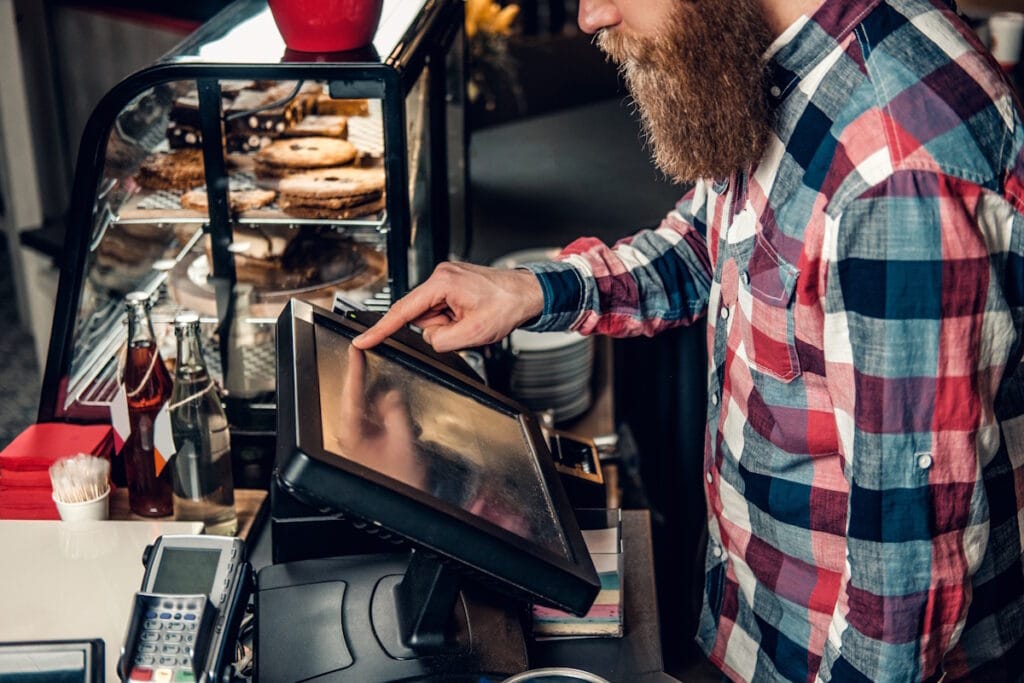 Patron barbu en chemise à carreaux tapant sur l'écran d'une caisse enregistreuse tactile