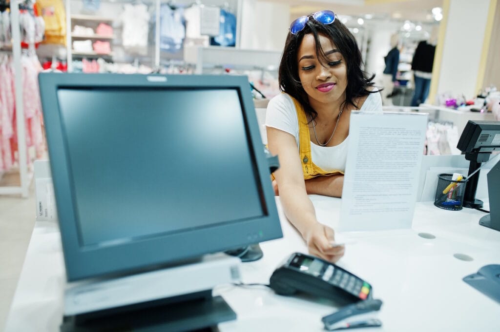 Jeune femme tendant le bras vers le TPE pour payer ses achats par carte bancaire
