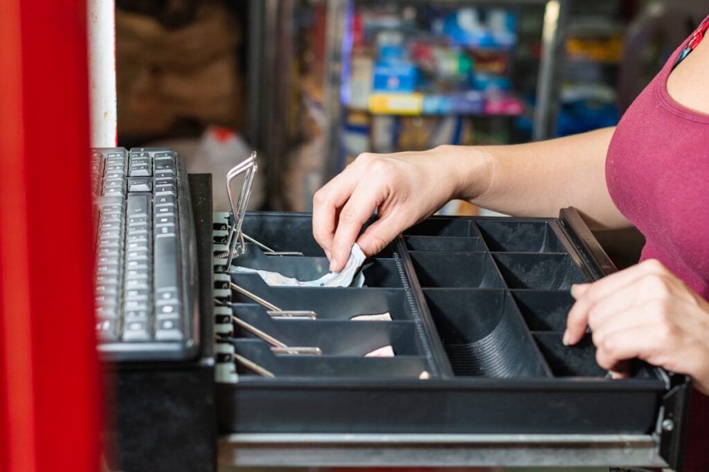 Gros plan d'une main rangeant des billets dans le tiroir d'une caisse enregistreuse