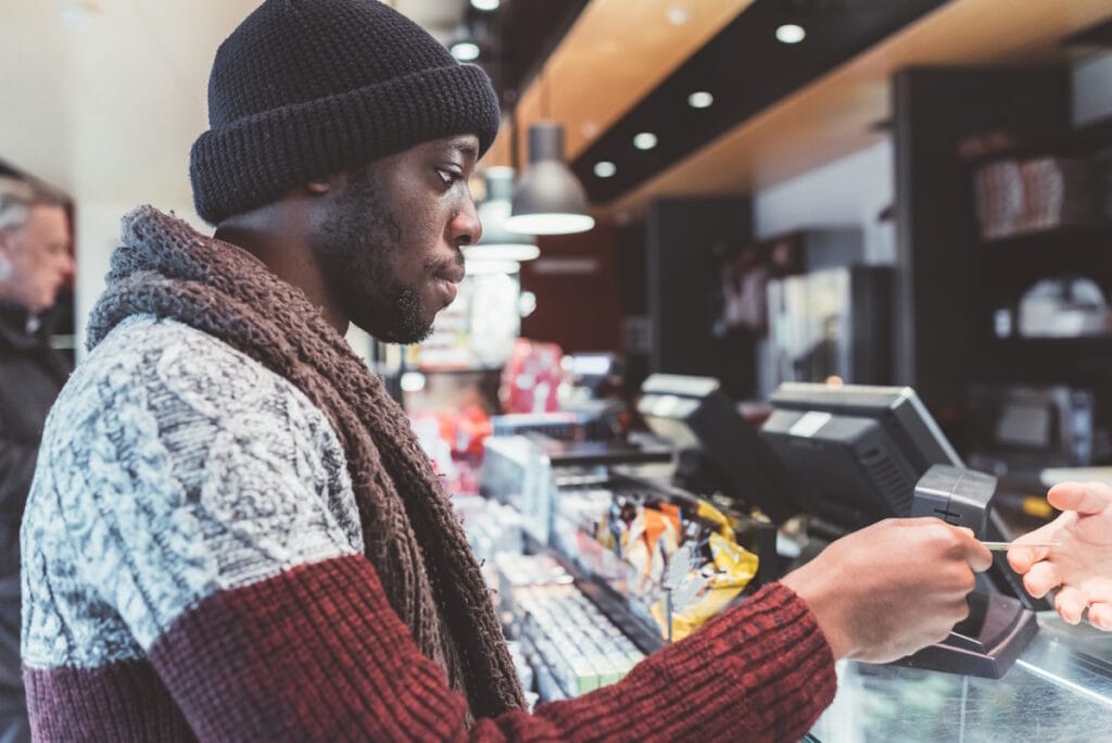 Jeune homme réglant ses achats devant un présentoir comportant plusieurs caisses tactiles