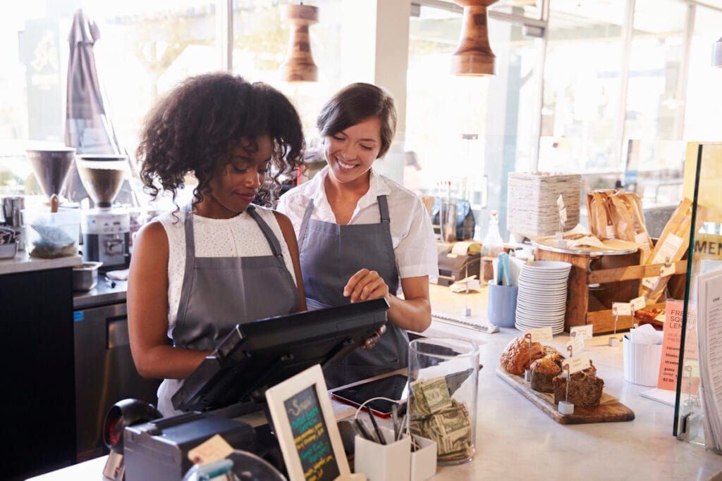 Deux jeunes commerçantes souriantes utilisant une caisse avec TPE intégré
